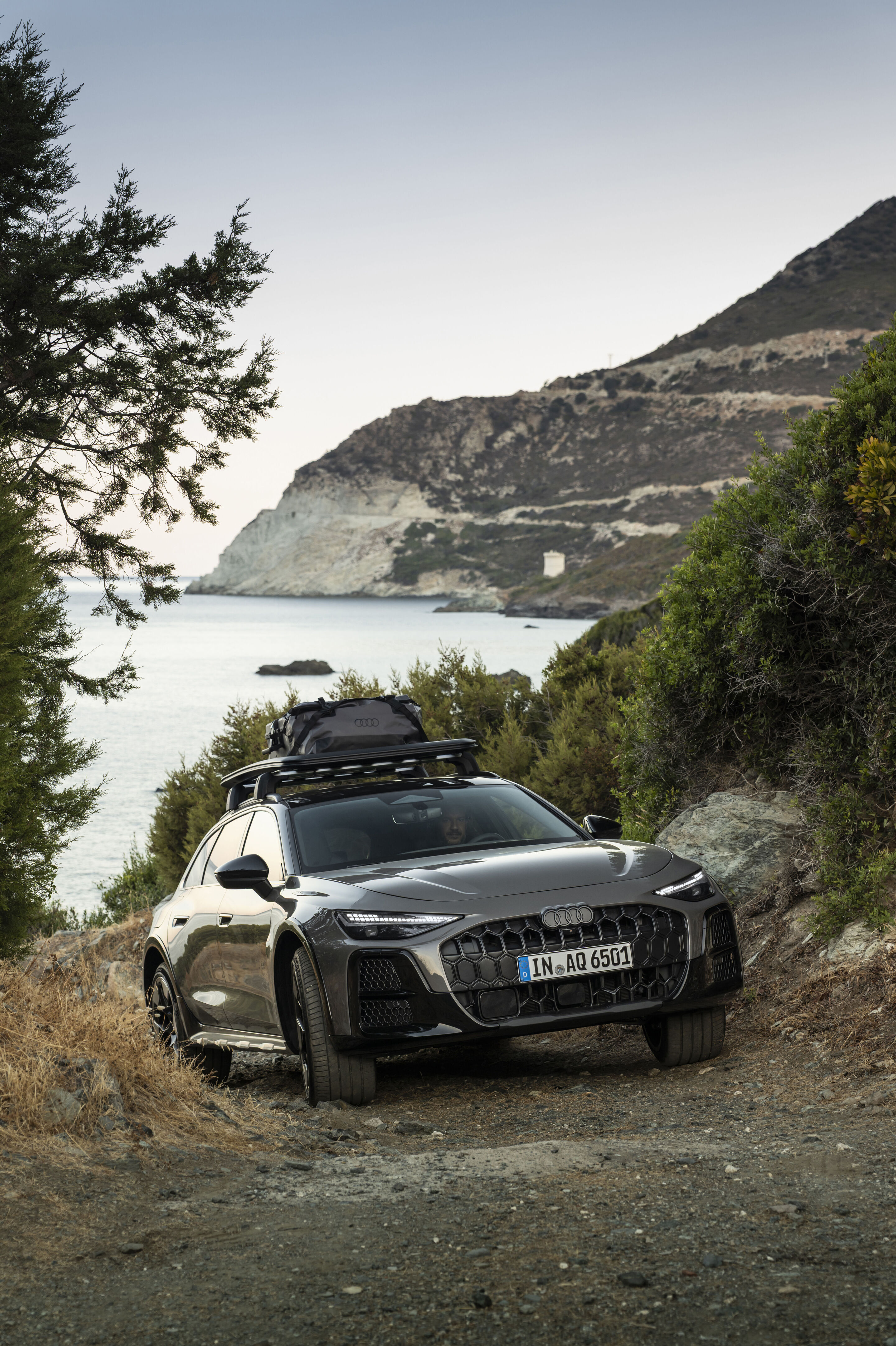 Audi A6 allroad TDI plateau grey metallic - Audi A6 allroad TDI in Plateau Gray metallic with roof box, outdoor driving shot, exterior, three-quarter front view in a mountainous setting.
