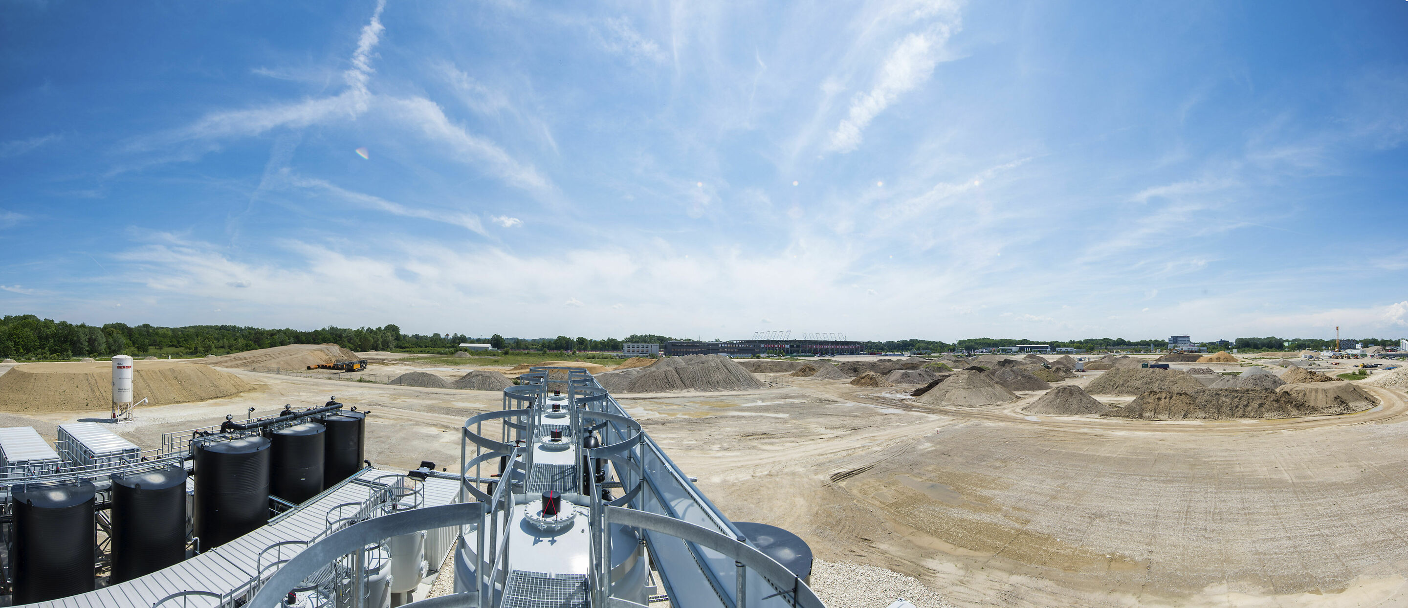 IN-Campus GmbH: Audi und Stadt Ingolstadt sanieren Raffineriegelände für Technologiepark - Blick von der Abstromsicherung über das Gelände mit Haufwerken von sauberem Boden zur Wiederverfüllung – im Hintergrund zu erkennen der Audi Sportpark