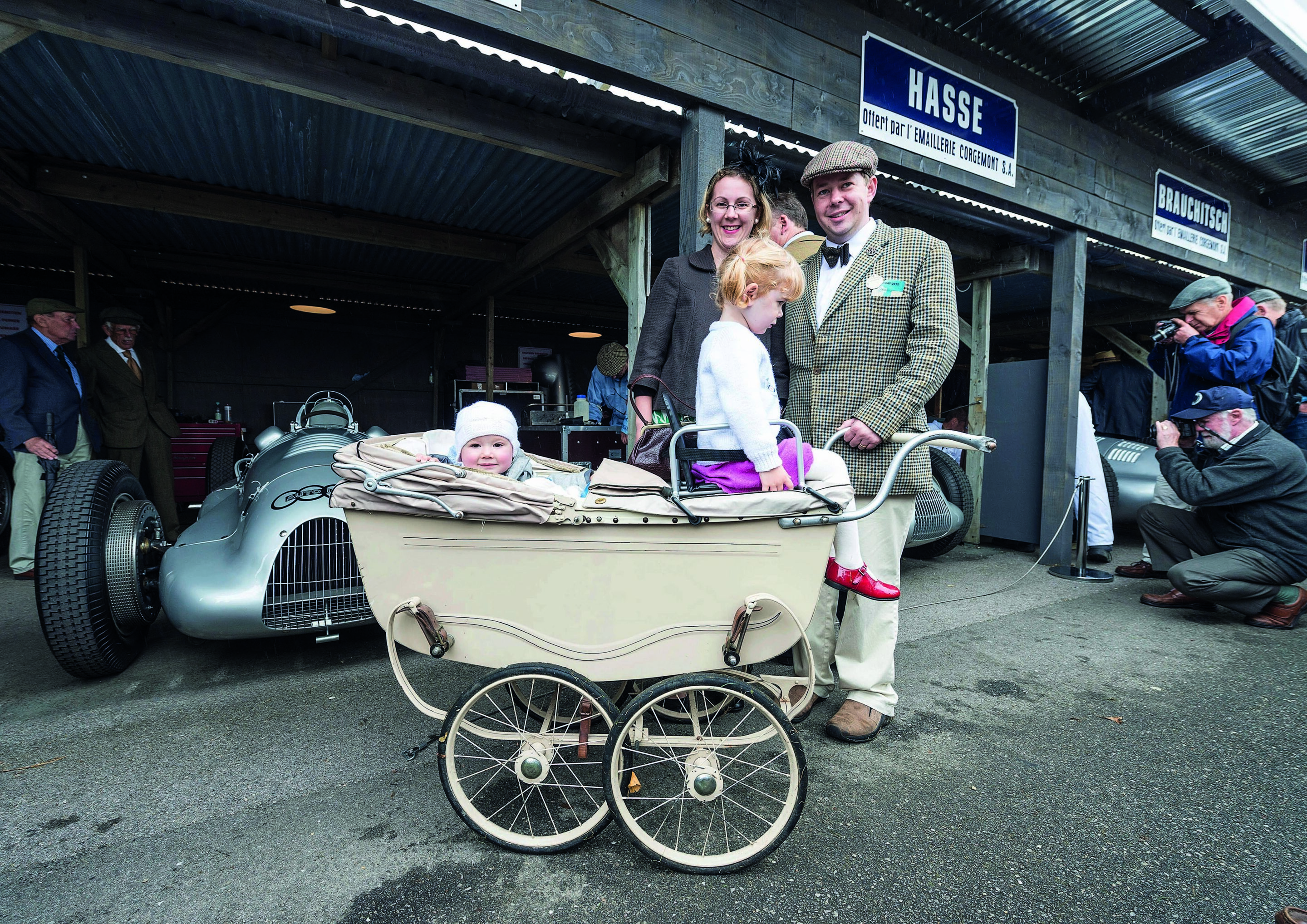 Audi Tradition beim Goodwood Revival - Familienereignis Goodwood Revival mit historischem Kinderwagen vor historischem Auto Union Rennwagen.